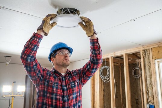 Electrician installing recessed ceiling light fixture in unfinished room. Concept of home improvement and renovation.