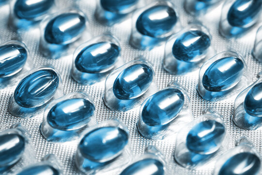 Blue gel capsules in blister packaging closeup texture. Transparent softgel pills arranged in pharmaceutical foil pack background. Medical industry and healthcare treatment pattern.