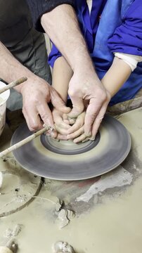 Adult and child making pottery together on wheel.