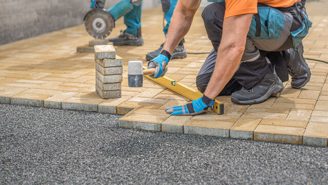 Laying of the interlocking paving. Worker compacting locking blocks in their laying bed using a rubber hammer.