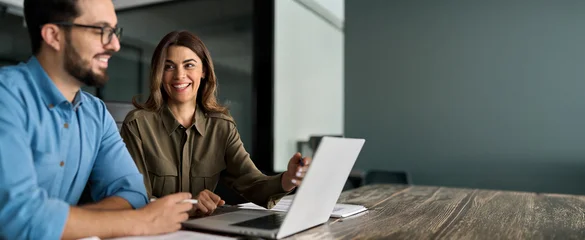 Selbstklebende Fototapeten Altes Krankenhaus Beelitz Happy busy female manager explaining corporate software work talking to young male employee consulting client working on computer using laptop discussing business project plan at office meeting.  © insta_photos