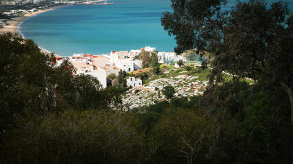Obraz premium Panoramic view over M’diq, turquoise Mediterranean beach, hillside cemetery and white houses framed by dense vegetation, northern Morocco.