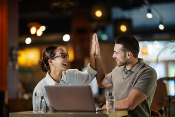 Coworkers celebrating success with a high five in coffee shop