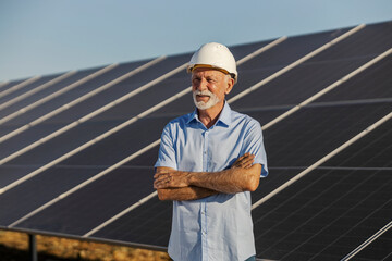 Senior male environmentalist wearing helmet standing confidently near solar panels on sunny day