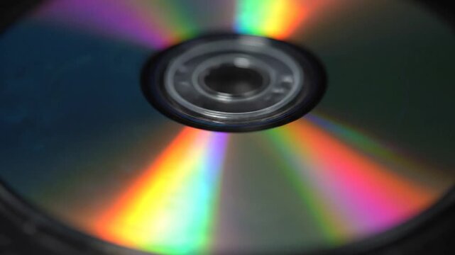 Mesmerizing close-up footage of an optical disc's reflective surface reveals shifting, vibrant rainbow diffraction patterns. Light refracts off the data layer, creating holographic colors that slight