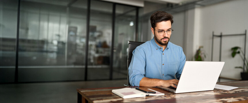 Busy professional business man company employee, young male worker software developer, latin businessman typing on computer technology using laptop searching on web working at office workplace desk.