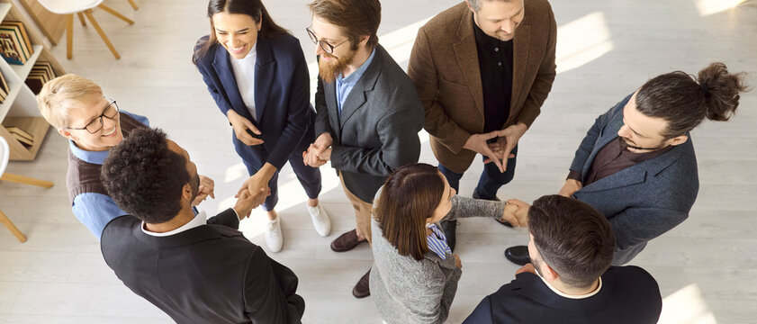 Businesspeople team meeting in office handshake. High angle view of a diverse group networking and greeting, sharing ideas in a bright workspace. Represents teamwork partnership trust and unity.