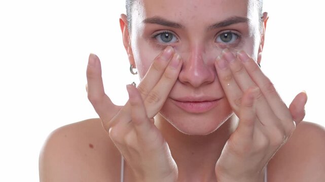 Young woman applying concealer under eyes with fingers, beauty skincare routine, studio shot on white background