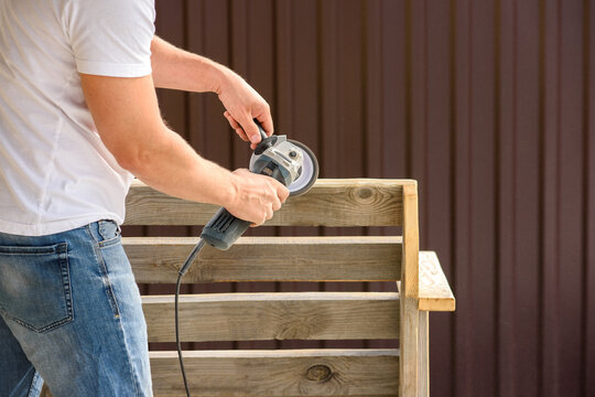 A man sand a homemade wooden bench with a angle grinder outdoor. Close up. DIY