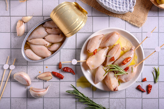 Gourmet canned small squids in olive oil with rosemary and chili peppers on a white plate, tapas