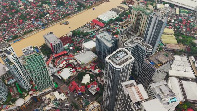 Brown river cuts through dense city towers as drone moves smoothly, Metro Manila
