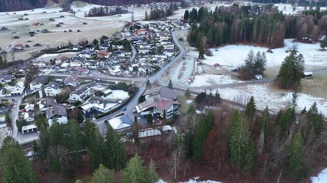 winding road threading through snow dusted meadows clustered alpine homes garmisch partenkirchen bordered by dense evergreen forests open winter fields reveals drone view garmisch-partenkirchen 