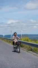 Smiling Asian child cycling along rural road near wind turbines, representing sustainable clean energy.