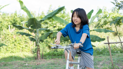 Young girl riding a bicycle on a sunny day surrounded by greenery.