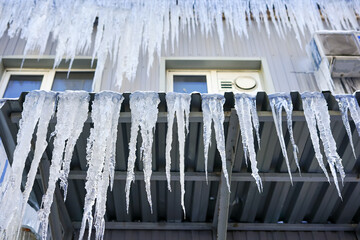Dangerous icicles hanging from a building roof and balcony in winter