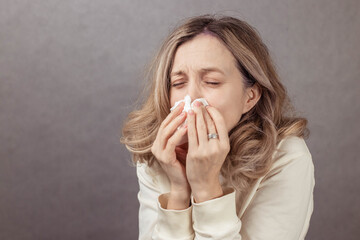 Female individual is holding tissues to her face, showing signs of discomfort in a softly lit...