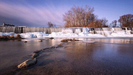 Winter weir at Cvrcovice with ice cascades in warm light. Long exposure creates a silky water effect amidst a frozen natural landscape. © Jana Krizova