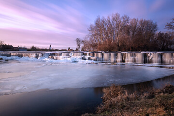 Winter weir at Cvrcovice with ice cascades in warm light. Long exposure creates a silky water effect amidst a frozen natural landscape. © Jana Krizova
