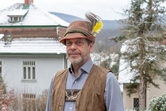 Adult man in Tyrolean hat and vest posing outdoors in winter in rural Europe