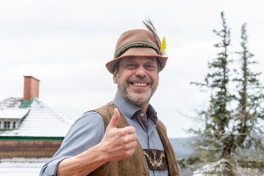 Adult man in Tyrolean hat and lederhose smiling and showing thumbs up in rural Austria