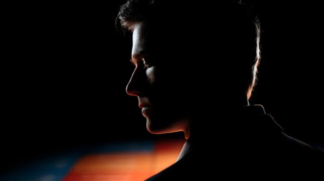 Dramatic side profile silhouette of a man illuminated by contrasting light against a blurred colorful background