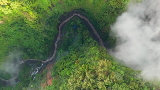 4K Sideways drone flight over Tumpak Sewu canyon in East Java Indonesia revealing a winding river, misty cliffs, lush jungle vegetation and soft morning light atmosphere.