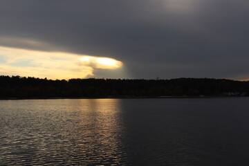Dark storm clouds opening with golden light over lake landscape