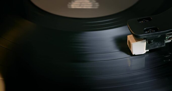 Detailed close-up of a turntable tonearm with white cartridge headshell, positioned over a black vinyl record on the platter, highlighting audio equipment precision.