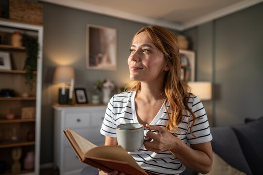 Woman relaxing at home reading book holding coffee mug