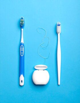 Overhead shot of dental hygiene items against a blue background, showcasing a toothbrush on each side and floss in between