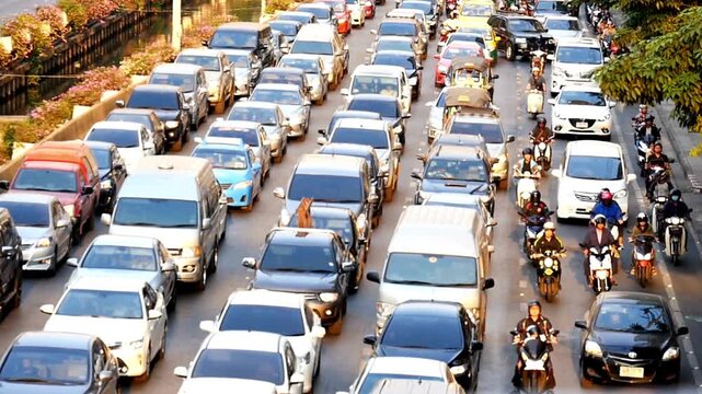 Busy street traffic jam with cars, motorcycles, and scooters moving slowly on a city road during the day, highlighting urban congestion and commute.
