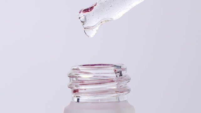 Cosmetics transparent liquid gel dripping from glass pipette into the bottle on white background