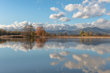 Fototapeta premium River with clouds and mountains under blue sky floods plain in autumn
