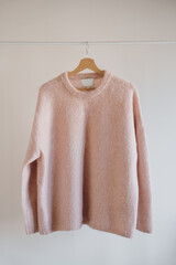 Cozy Pink Knitted Wool Sweater Hanging On Wooden Hanger Against Plain White Wall