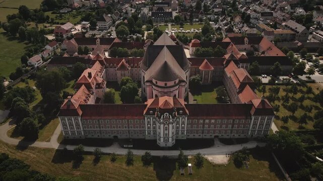 Smooth 4K drone pullback from Kloster Wiblingen in Ulm while the camera tilts up, revealing the full monastery complex, surrounding town rooftops, and expansive sky.