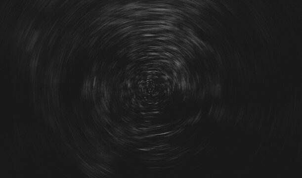 Abstract dark circular motion texture with radial blur effect. Black grunge background featuring subtle light streaks forming a vortex pattern, creating a dynamic and dramatic backdrop with centered c