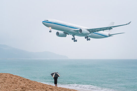 Flight trip to Phuket in Thailand rainy season. A plane flying low over the sea lands at the airport on the island, a vacationing tourist with an umbrella on beach meets plane. Vacation in Thailand