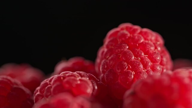 Macro shot of fresh raspberries as camera slides from left to right across a heap of berries. Rich red texture and soft light create depth, contrast and premium food advertising concept.
