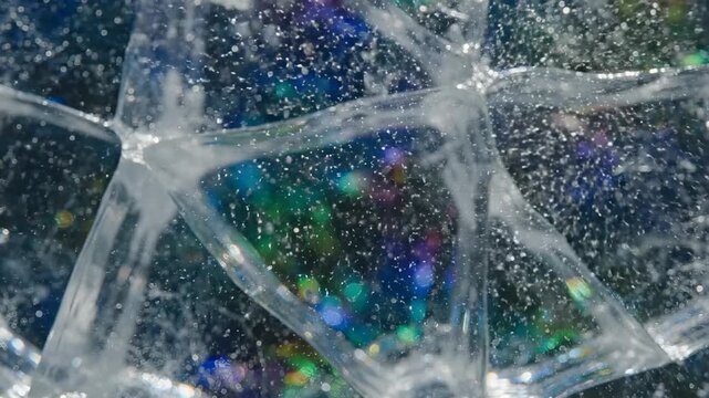 Close-up of cracked ice with colorful reflections. The surface shows intricate patterns and a mix of blue, green, and purple hues.