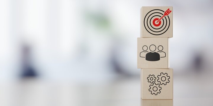 Stack of wooden blocks with team, process and goal or target icons on table in front of office background with selective focus and copy space, business process or achievement concept
