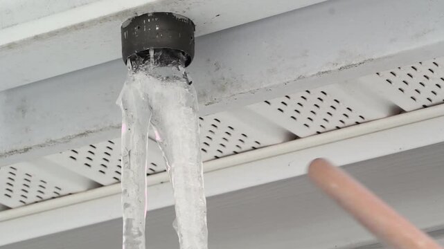 Knocking off an icicle from a house gutter drain, showing ice buildup and cold-weather maintenance and safety issue.