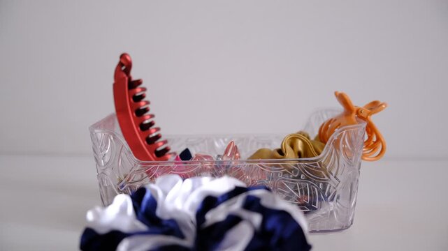 Woman hair accessories, plastic claw clips featuring multiple gripping prongs for securing hair, hair scrunchies falling in box. background with copy space. Trendy fashionable accessory.
