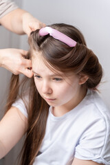 Fototapeta premium Mom's hands twist curlers for daughter in white T-shirt at home on a light background in front of the mirror