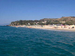 Beautiful panoramic view of the Calabrian coast during the summer season, featuring turquoise crystal-clear waters, dramatic rocky cliffs, and charming seaside scenery under bright blue skies. The