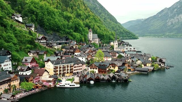 Aerial drone footage of Hallstatt, Austria, showing the picturesque alpine village, lake shoreline, historic buildings, and surrounding mountains.
