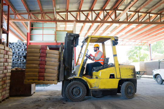 Forklift driver moving cement bags on pallet in warehouse, managing construction supply logistics and industrial inventory
