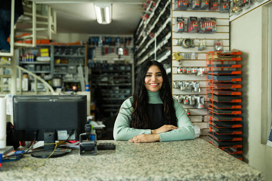 Female small business owner standing at counter, smiling, working in a professional hardware store or retail shop