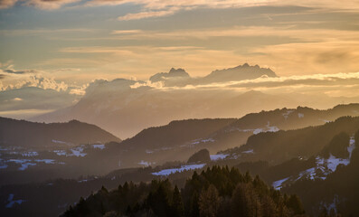 Alpine winter landscape in Bregenzer Wald at sunset with snow-covered mountains and Saentis summit  glowing in warm evening light under a dramatic sky. Austria, Vorarlberg