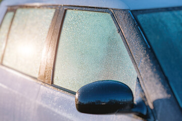 Car windows and side mirror covered frost and dew, reflecting morning sunlight during a cold day