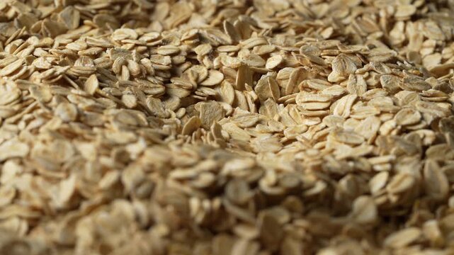 Dry oat flakes background, close up, rotation. Uncooked raw oat flakes grains. Healthy breakfast and diet eating ingredients for making oatmeal porridge. Gastronomy concept, organic food